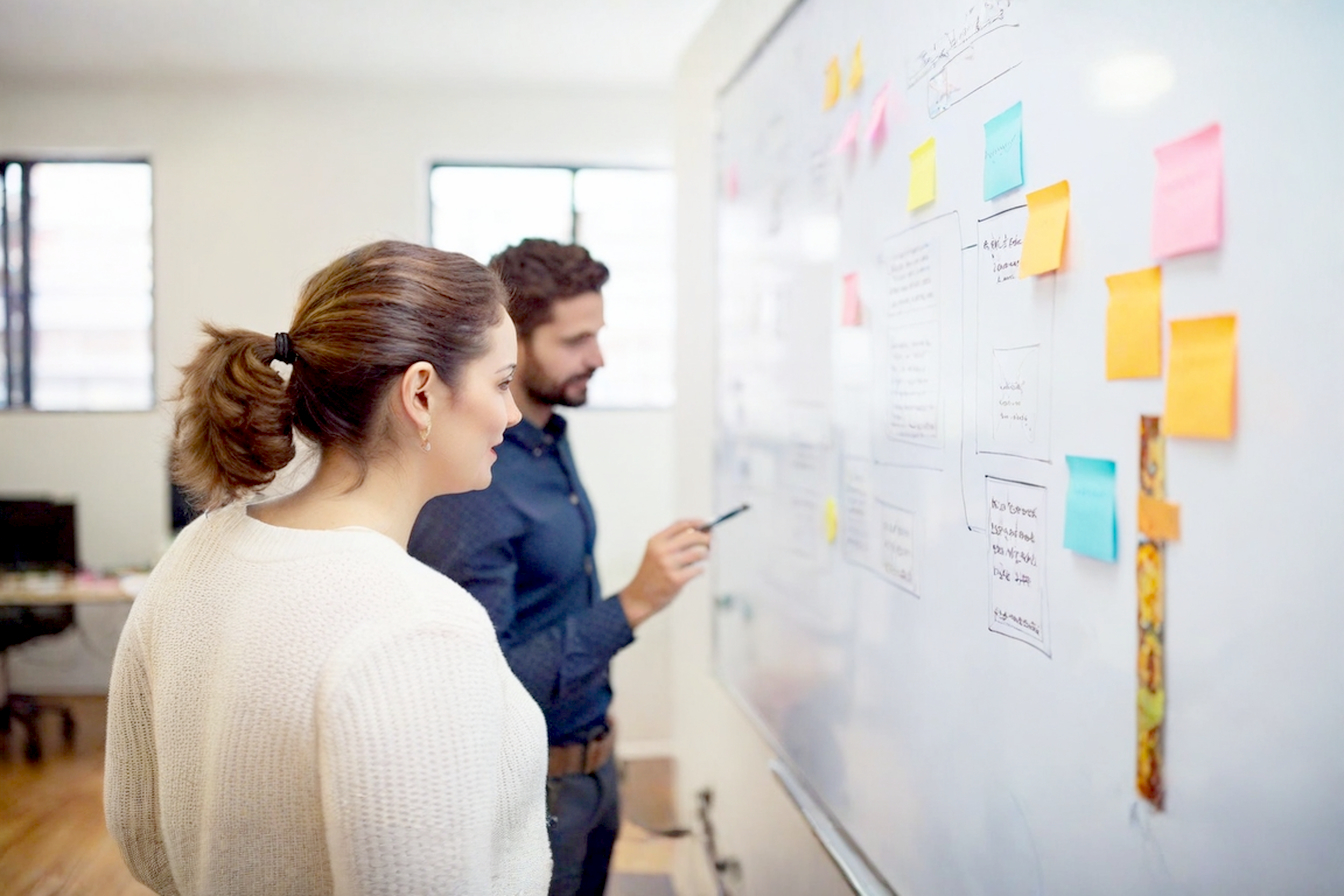 Professional, lifelike photograph depicting a marketing team collaboratively sketching out a customer journey map on a large whiteboard. The map shows clear stages (Awareness, Interest, Decision, Action, Loyalty) with email icons at each stage, symbolizing an email marketing funnel. The team looks engaged and optimistic. Soft, natural office lighting. Focus on the whiteboard and the concept of a strategic journey. Modern, clean aesthetic.