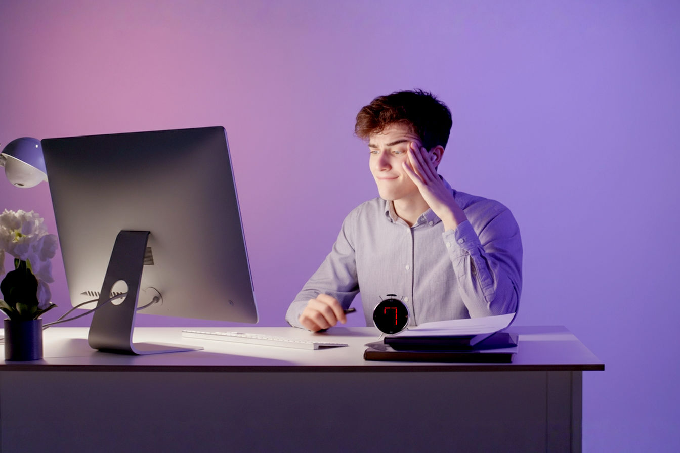 Professional, lifelike photo: A stressed person at a modern, slightly cluttered desk looks relieved and smiles faintly as they look at a concise, well-structured document (clearly a press release draft) on their computer screen. A physical timer on the desk shows '7 MIN'. Soft, encouraging light. Focus on the transition from stress to relief/accomplishment. Minimalist background.