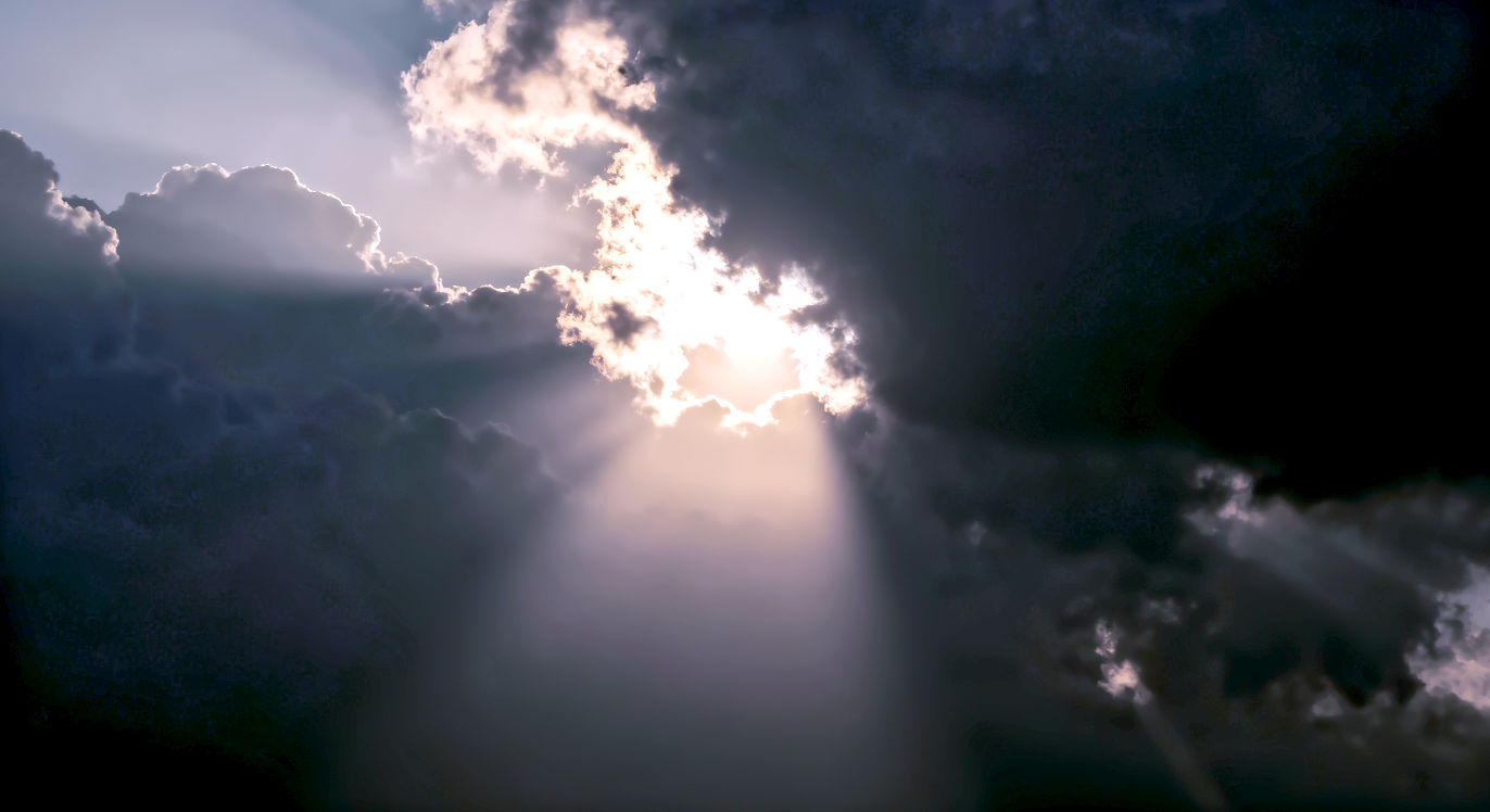 Abstract, 16:9. A dark, moody sky with a single, powerful ray of sun breaking through the clouds. Mood: Dramatic, Hope.
