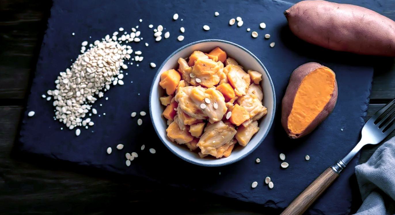 Professional DSLR photo, 16:9, bright overhead (flat lay) shot. Subject: A composition of whole-food "fuel" ingredients. Foreground: Cooked chicken, a scoop of dry oats in a simple bowl, and a whole sweet potato, arranged artfully. Background: A clean, dark slate cutting board or wooden table. Mood: Wholesome Note: NO text, NO abstract graphics. No people. The focus is on the raw, unprocessed "bricks" for muscle building.