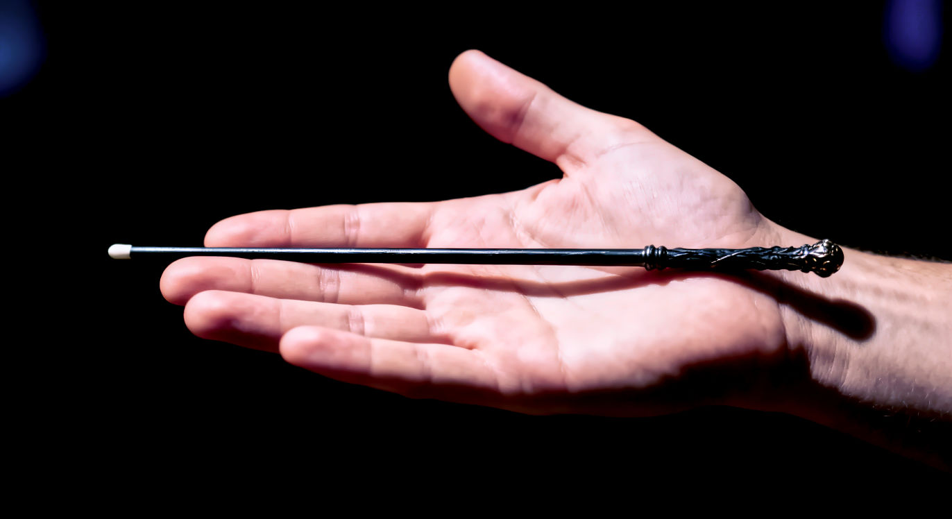 Professional DSLR photo, 16:9, dramatic, focused light. Subject: A person's hand, palm up, holding out a single, metaphorical "magic wand" (a simple, elegant stick) that is clearly not sparking or magical. Foreground: The hand and the non-magical wand are in sharp focus. Background: A dark, unfocused background to isolate the subject. Mood: Cautionary Note: NO text. The image should convey the idea of someone expecting a "magic wand" solution, which the article warns against.